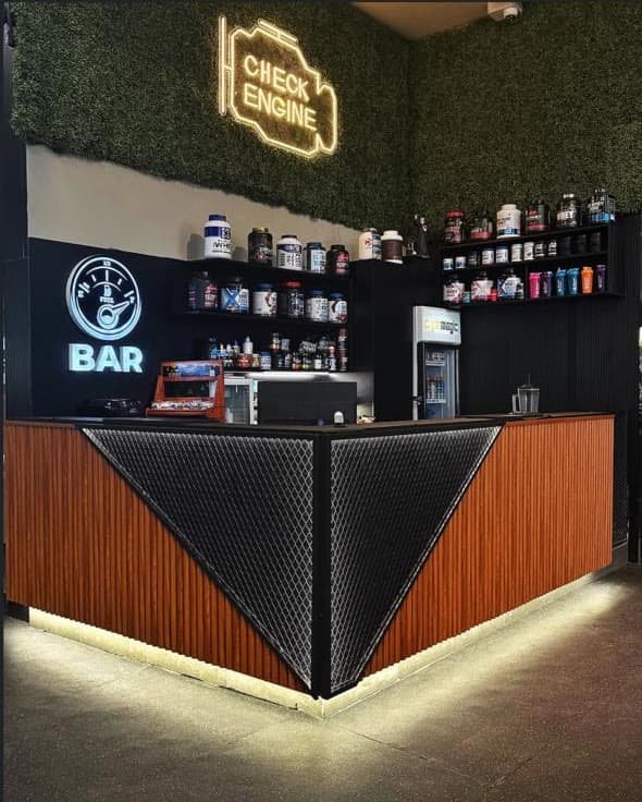 The Fuel Bar at Gymmagic with supplement shelves under a Check Engine neon sign